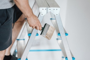 A person ascending a ladder while holding a paintbrush.