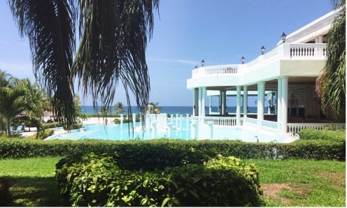 A large white house with a pool and lots of greenery.