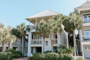 A white and beige house near green trees under a blue sky.