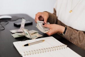 A woman counting money above a notebook